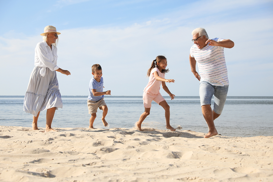 Nonni passeggiano sulla spiaggia con i nipoti, durante una vacanza al mare
